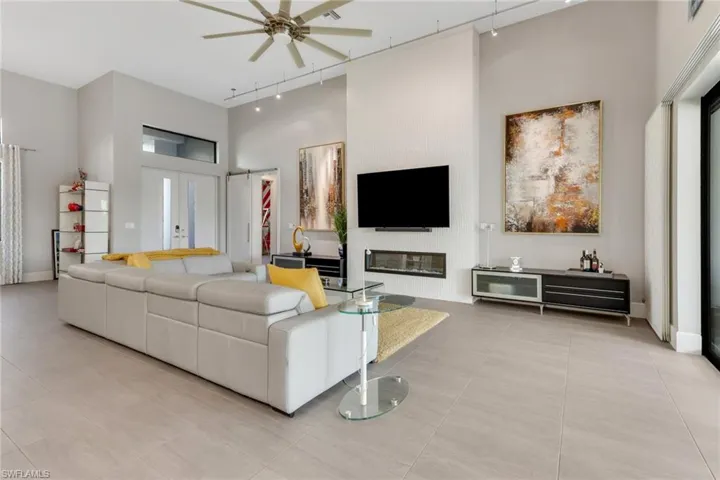 Living room with rail lighting, a high ceiling, ceiling fan, light tile patterned flooring, and french doors