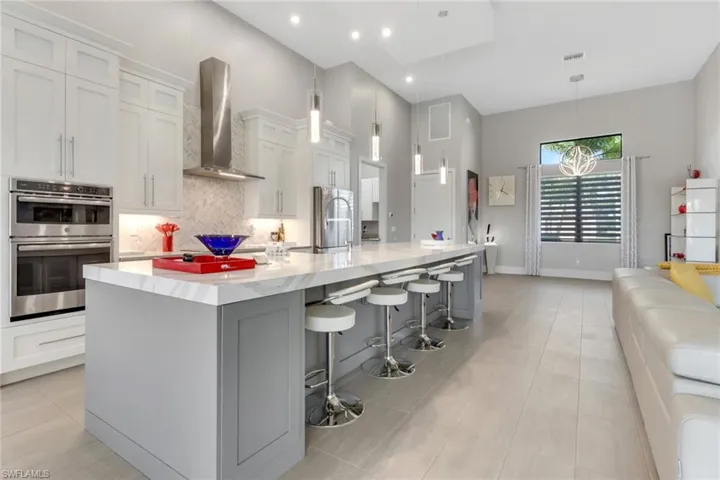 Kitchen with backsplash, a spacious island, stainless steel appliances, wall chimney range hood, and a kitchen bar