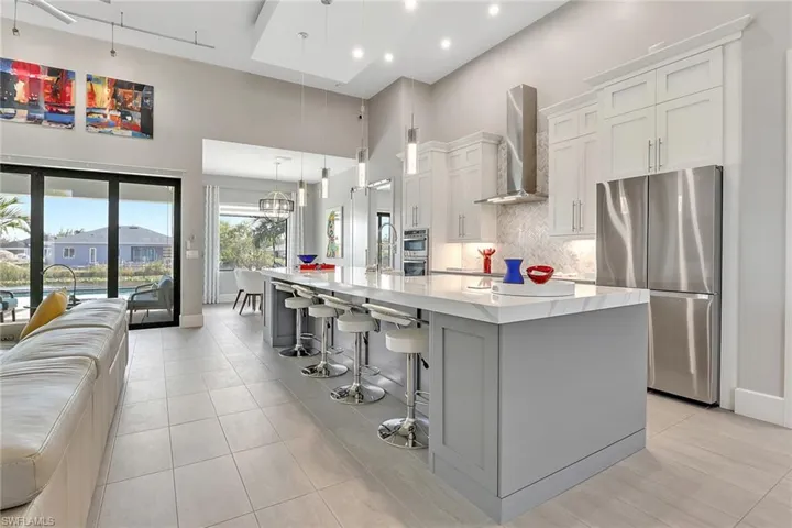 Kitchen featuring stainless steel appliances, backsplash, white cabinets, wall chimney range hood, and a spacious island