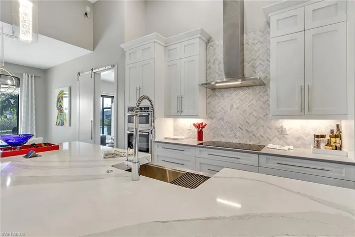 Kitchen featuring wall chimney exhaust hood, a barn door, decorative backsplash, white cabinetry, and light stone countertops