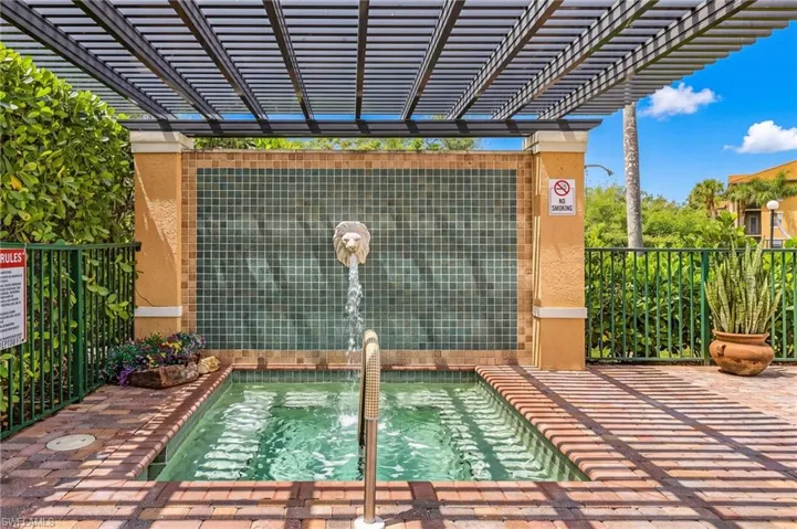 Water feature with a lion's head spigot, tiled backdrop, and brick paver surround