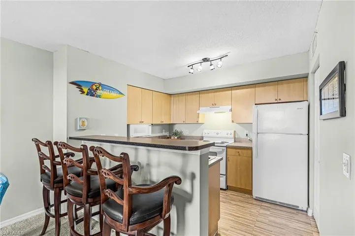 Compact kitchen featuring light wood-finish cabinetry, white appliances, and a breakfast bar with a dark countertop