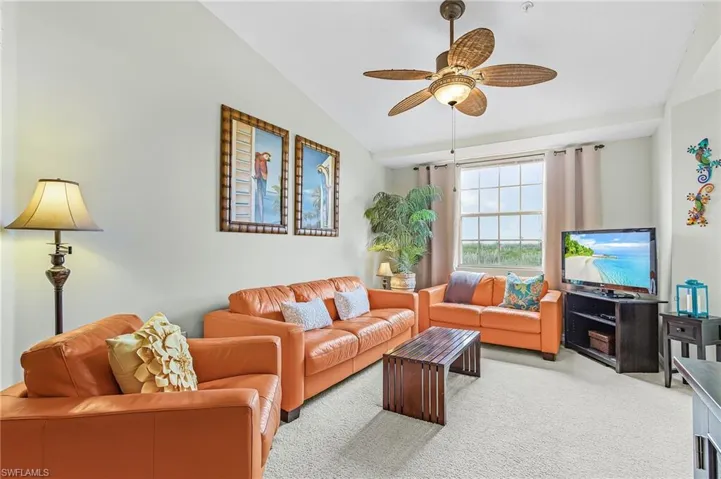Vaulted ceiling with an integrated ceiling fan, carpeted flooring, and a large window with vertical blinds