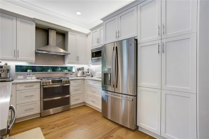 Kitchen featuring stainless steel appliances, wall chimney exhaust hood, light countertops, light wood-type flooring, and recessed lighting