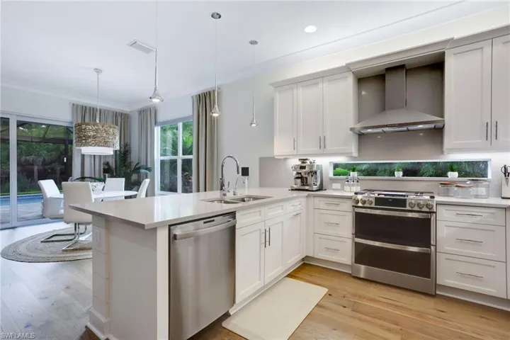 Kitchen with stainless steel appliances, wall chimney exhaust hood, a sink, light countertops, and a peninsula