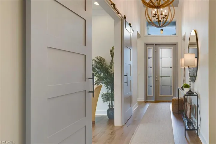 Entrance foyer featuring light wood-style floors, a chandelier, a barn door, and baseboards