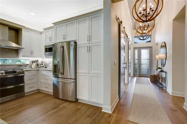 Kitchen with appliances with stainless steel finishes, a chandelier, wall chimney range hood, light wood-style flooring, and recessed lighting