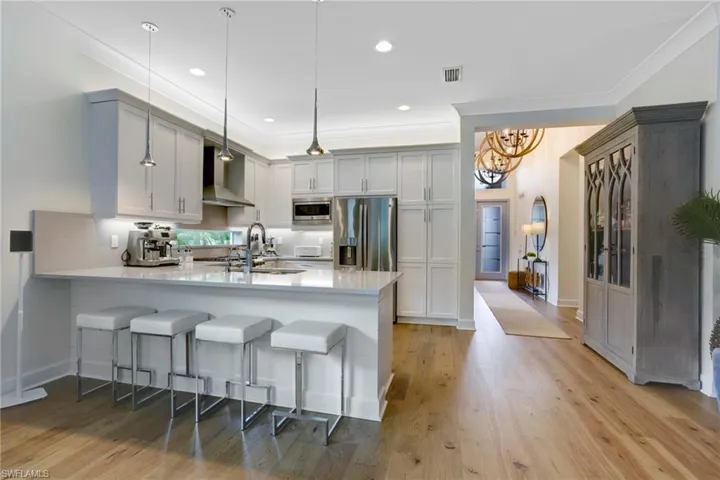 Kitchen featuring stainless steel appliances, a peninsula, a sink, light countertops, and a kitchen breakfast bar