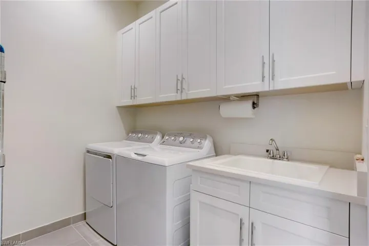Laundry room featuring washer and dryer, cabinet space, light tile patterned flooring, and baseboards