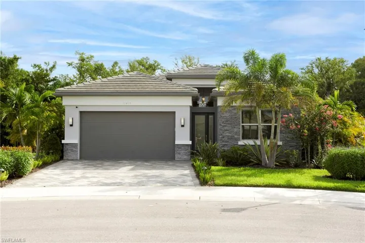 View of front facade with stone siding, a garage, driveway, stucco siding, and a tiled roof