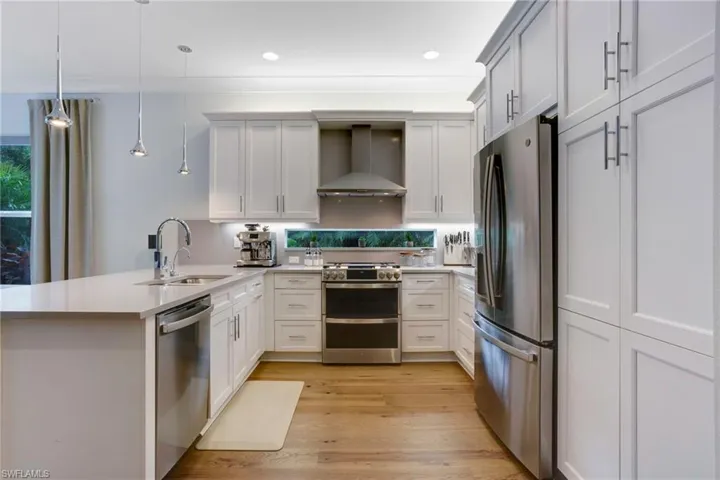 Kitchen with stainless steel appliances, wall chimney exhaust hood, a sink, a peninsula, and light countertops