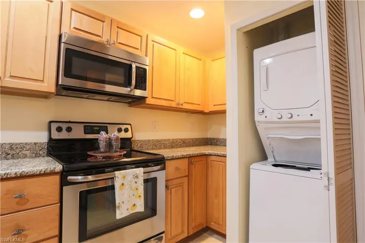 Kitchen with appliances with stainless steel finishes, light stone countertops, stacked washer / dryer, recessed lighting, and light brown cabinetry