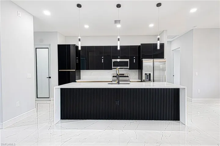 Modern kitchen featuring black cabinetry, stainless steel appliances, a large island with a white countertop, and contemporary pendant lighting