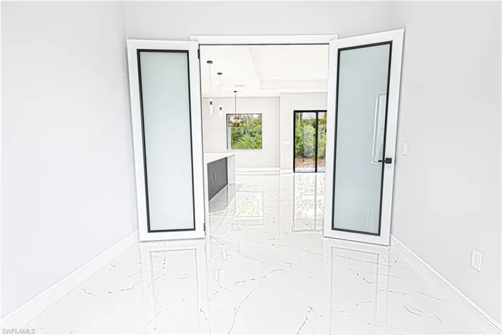 Entryway with white walls and polished marble flooring, featuring double doors with frosted glass panels and black trim
