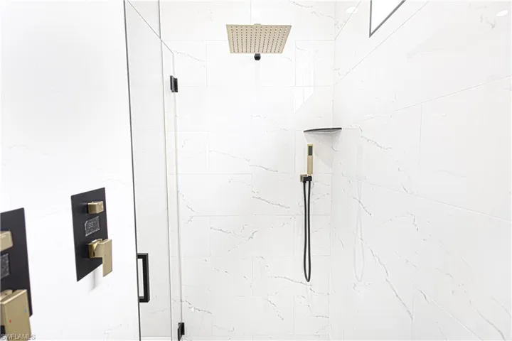 Shower featuring white tiled walls, a square rainfall showerhead, and a handheld shower attachment