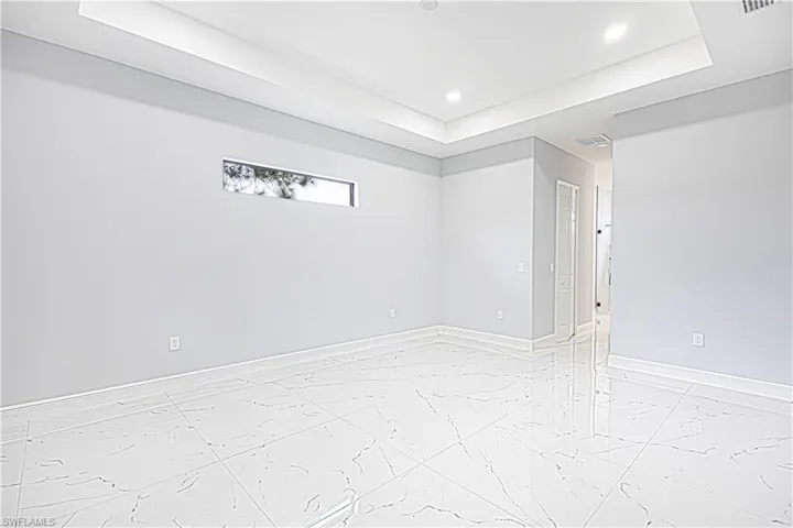Spacious room featuring white tile flooring, light-toned walls, a tray ceiling with recessed lighting, and a horizontal window
