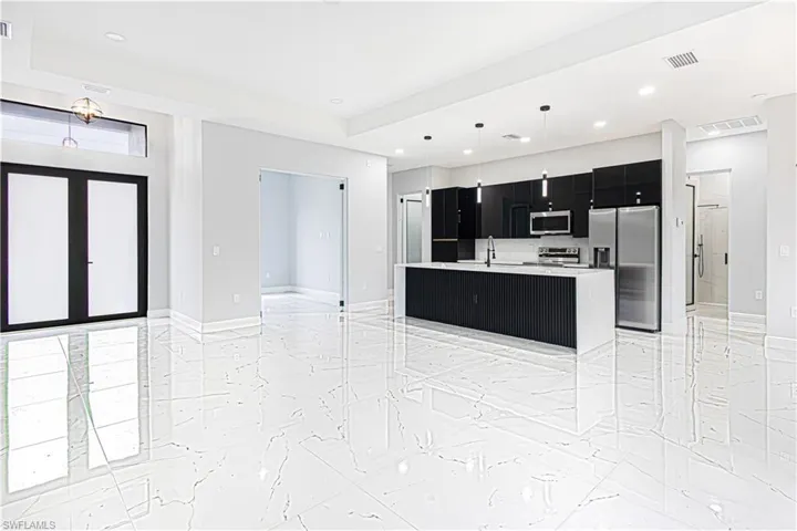 Open concept living space featuring white tiled floors, a contemporary kitchen with black cabinetry, a large island with a white countertop, and stainless steel appliances