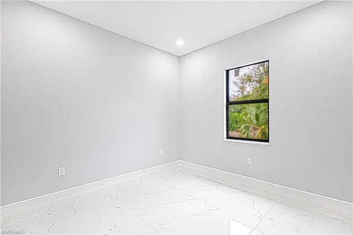 The room features a window providing views of lush greenery, recessed lighting, and white tile flooring with dark veining