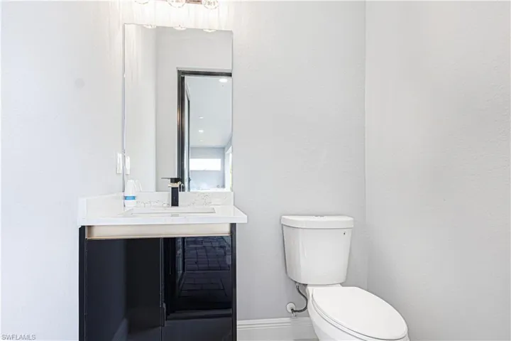 The bathroom features a vanity with a white countertop and a black cabinet, a rectangular mirror, and a white toilet
