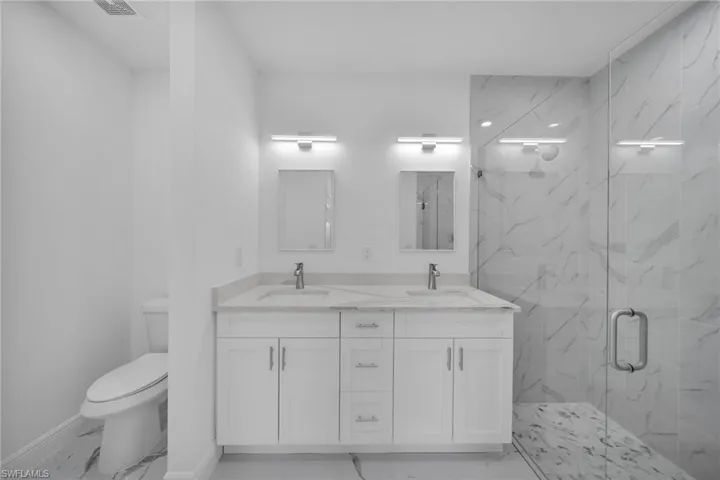 Full bathroom featuring double vanity, a marble finish shower, and marble finish floors