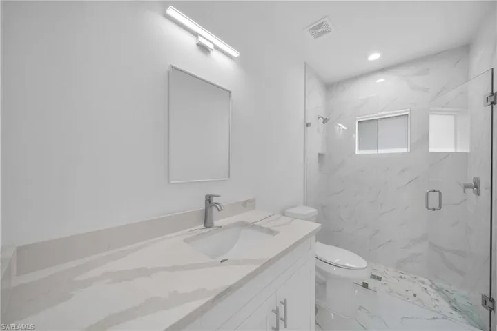 Bathroom featuring vanity, a marble finish shower, marble look tile flooring, and recessed lighting