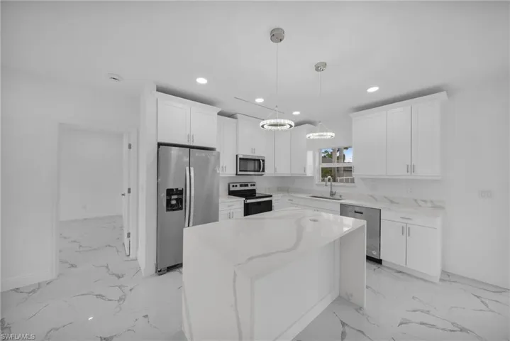 Kitchen featuring appliances with stainless steel finishes, recessed lighting, light marble finish flooring, white cabinetry, and a chandelier