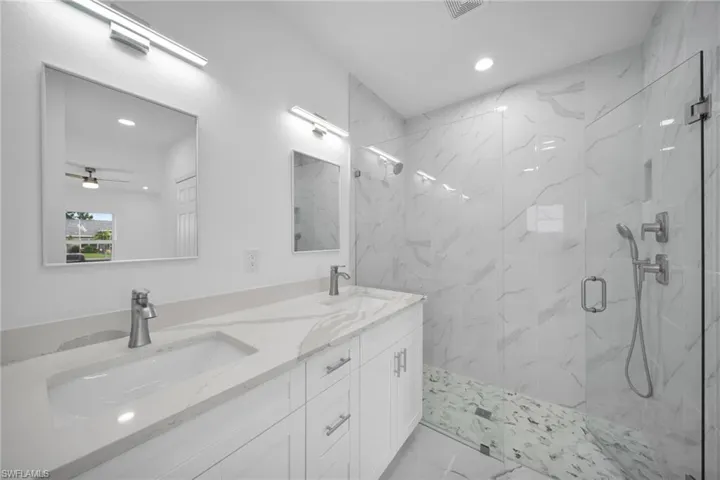 Bathroom with marble look tile flooring, recessed lighting, a marble finish shower, double vanity, and ceiling fan