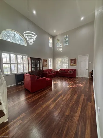 Living room featuring dark wood-type flooring, a chandelier, a towering ceiling, and recessed lighting