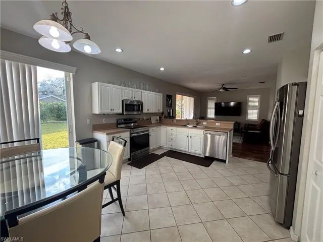 Kitchen featuring a peninsula, white cabinetry, stainless steel appliances, light tile patterned flooring, and healthy amount of natural light