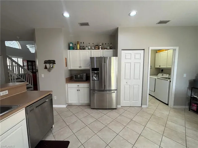 Kitchen featuring appliances with stainless steel finishes, light tile patterned floors, white cabinets, recessed lighting, and washing machine and clothes dryer