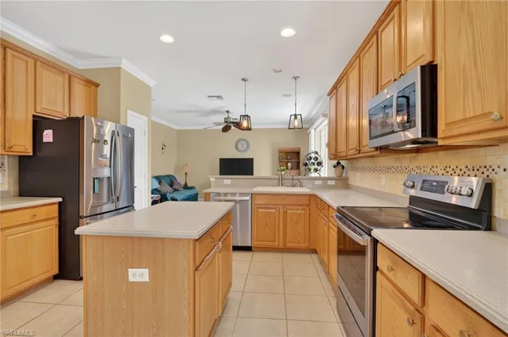 Kitchen with stainless steel appliances, crown molding, backsplash, pendant lighting, and light countertops