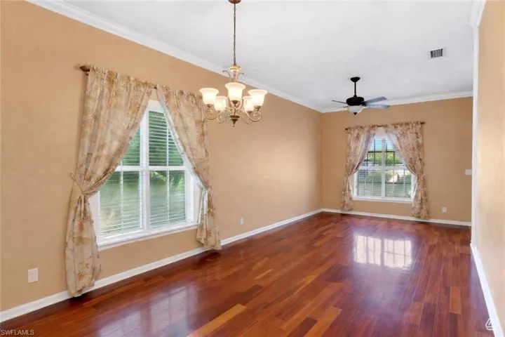 Spacious interior with rich wood-finish flooring, a decorative chandelier, and crown molding