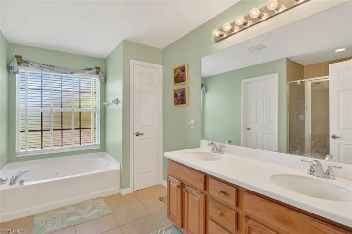 Full bathroom with light tile patterned floors, a tub with jets, double vanity, and a shower stall