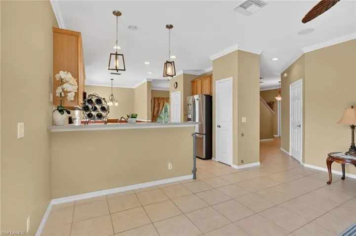 Kitchen with a peninsula, stainless steel fridge, decorative light fixtures, crown molding, and light countertops
