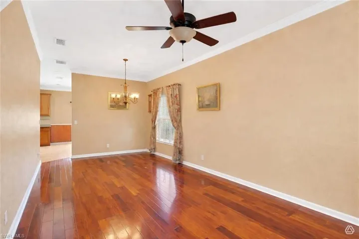 Spacious interior room featuring polished wood-finish flooring, a contemporary ceiling fan, and a brass-tone chandelier