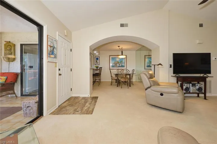 Living room featuring arched walkways, carpet, and vaulted ceiling