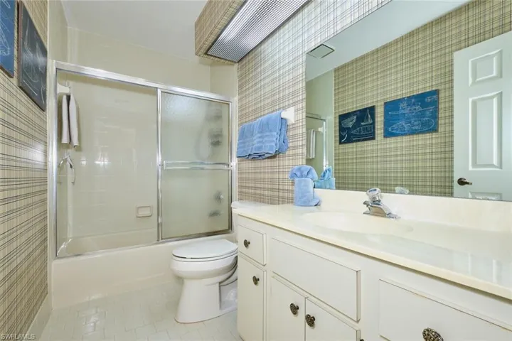 Full bath with vanity, light tile patterned flooring, combined bath / shower with glass door, and tile walls