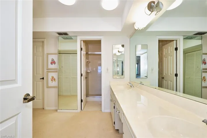 Full bathroom with double vanity, a closet, light colored carpet, and a shower with door