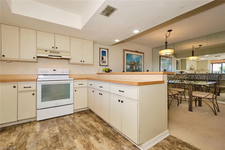 Kitchen with electric stove, a peninsula, light countertops, hanging light fixtures, and under cabinet range hood