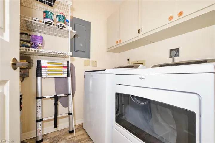 Laundry area with cabinet space, electric panel, washer and dryer, and light wood-style flooring