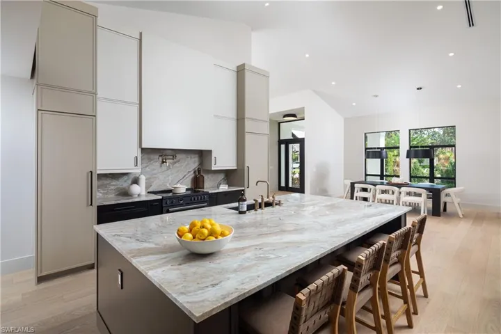 Kitchen with sink, light stone counters, backsplash, a kitchen bar, and a center island with sink