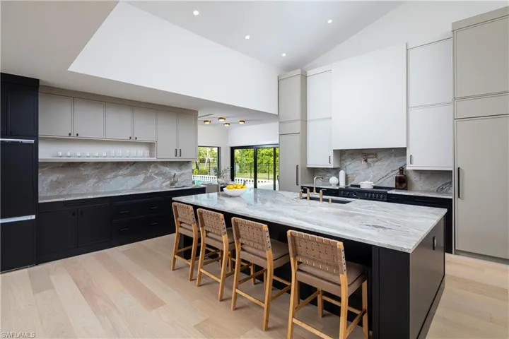 Kitchen with a kitchen island with sink, white cabinets, light stone countertops, light wood-type flooring, and a breakfast bar area