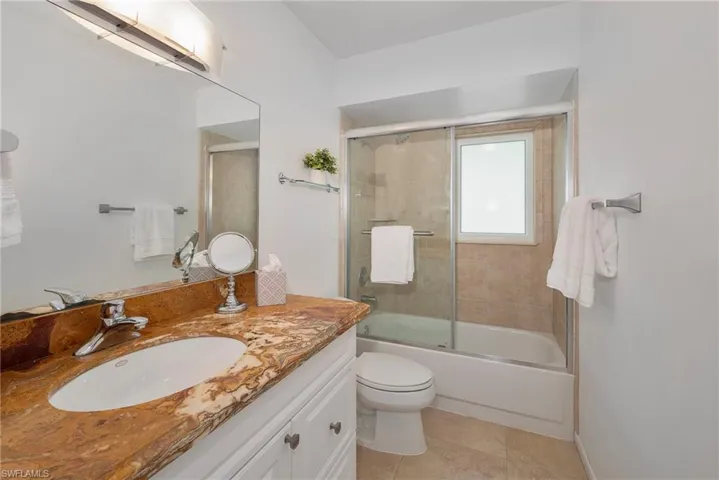 Full bathroom with tile patterned floors, vanity, bath / shower combo with glass door, and toilet