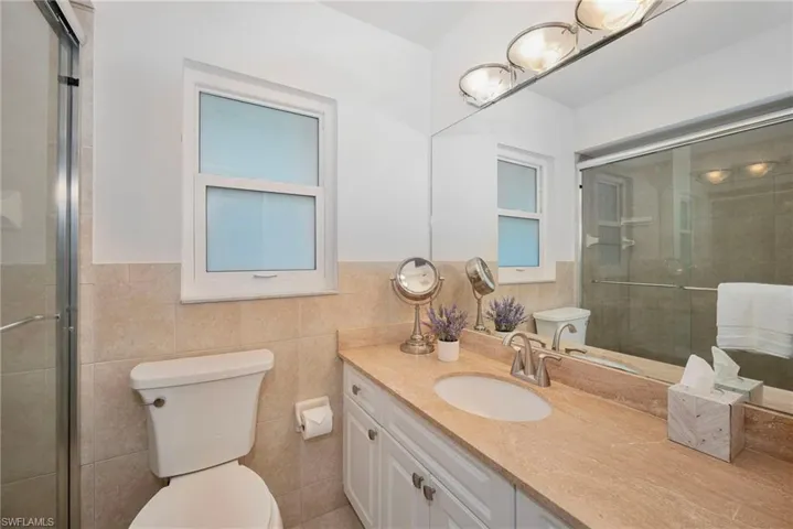 Bathroom featuring a shower with door, vanity, tile walls, and toilet