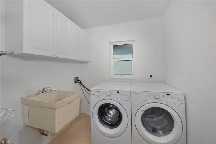 Laundry area featuring washing machine and clothes dryer, sink, light tile patterned flooring, and cabinets