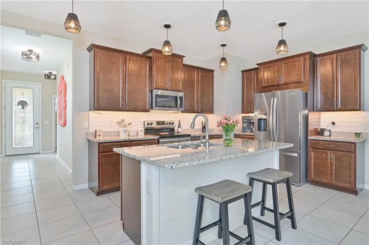 Kitchen with backsplash, light stone countertops, stainless steel appliances, and light tile patterned floors