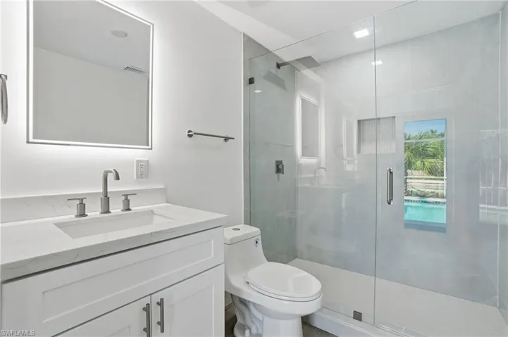 Contemporary bathroom featuring a frameless glass shower enclosure, integrated shower niche with hexagonal tile, and a vanity with a white countertop and rectangular sink