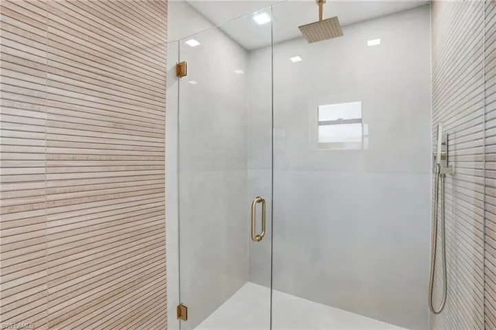 Glass-enclosed shower featuring a brass rain shower head, handheld shower fixture, and a window