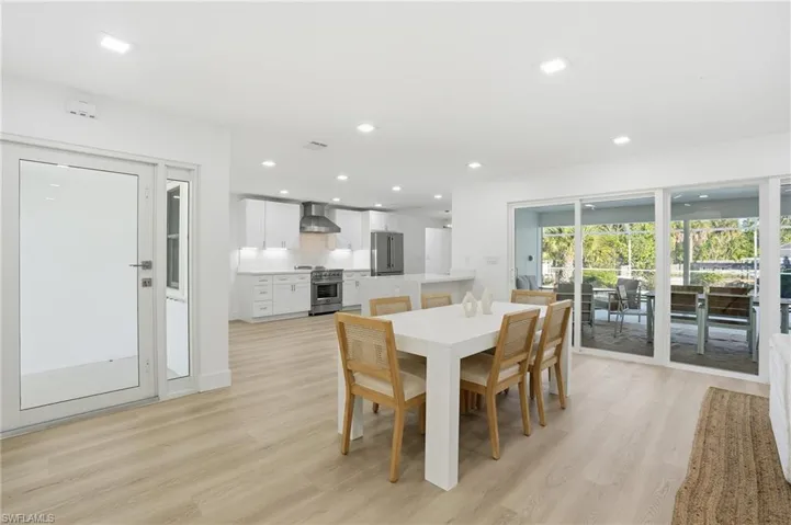 Open-concept living space featuring wood-finish flooring, a contemporary kitchen with stainless steel appliances, white cabinetry, and recessed lighting, and a full wall of sliding glass doors opening to the exterior