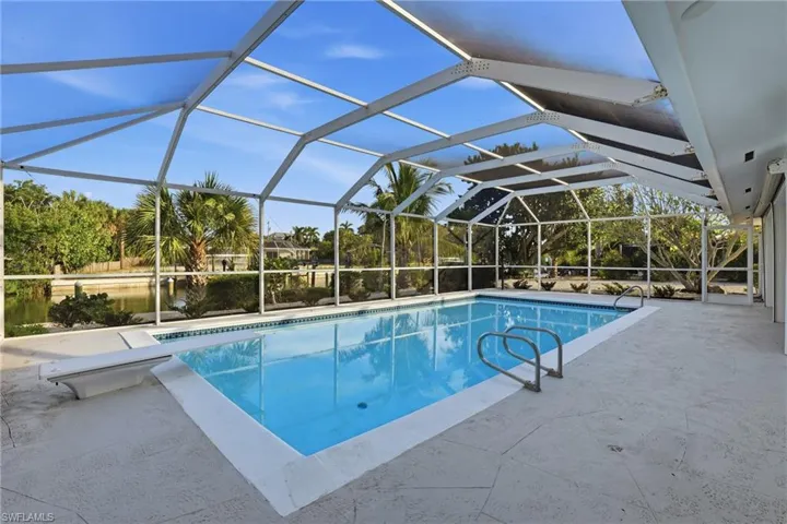 Screened outdoor pool with concrete decking, a diving board, and integrated pool steps
